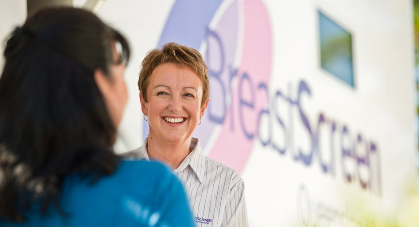 Female BreastScreen Queensland technician smiles at a female patient on the stairwell of a mobile service truck.